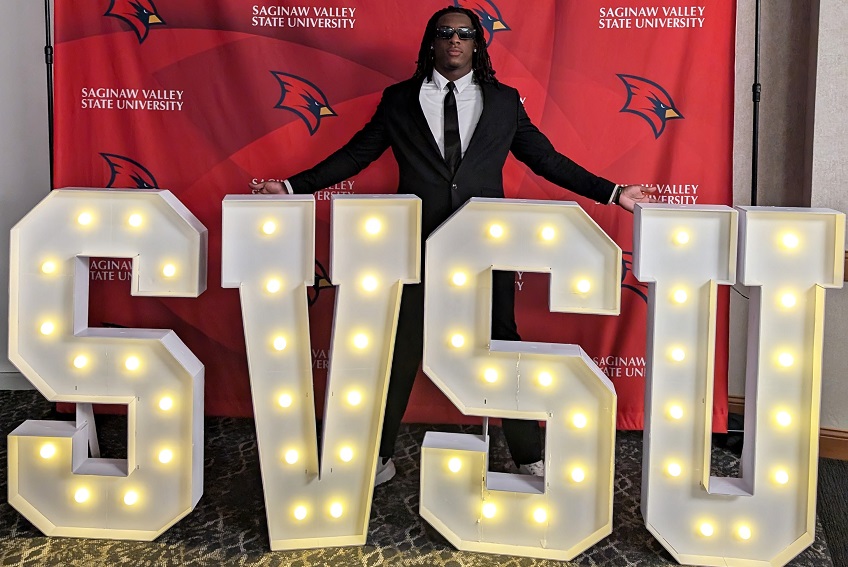 graduate posing behind the SVSU sign at Senior Toast