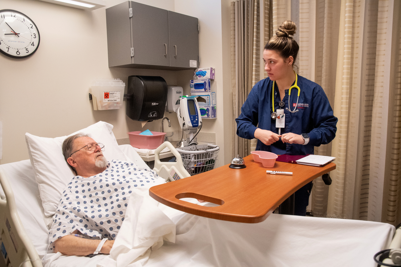 Young woman in blue scrubs with man in hospital bed